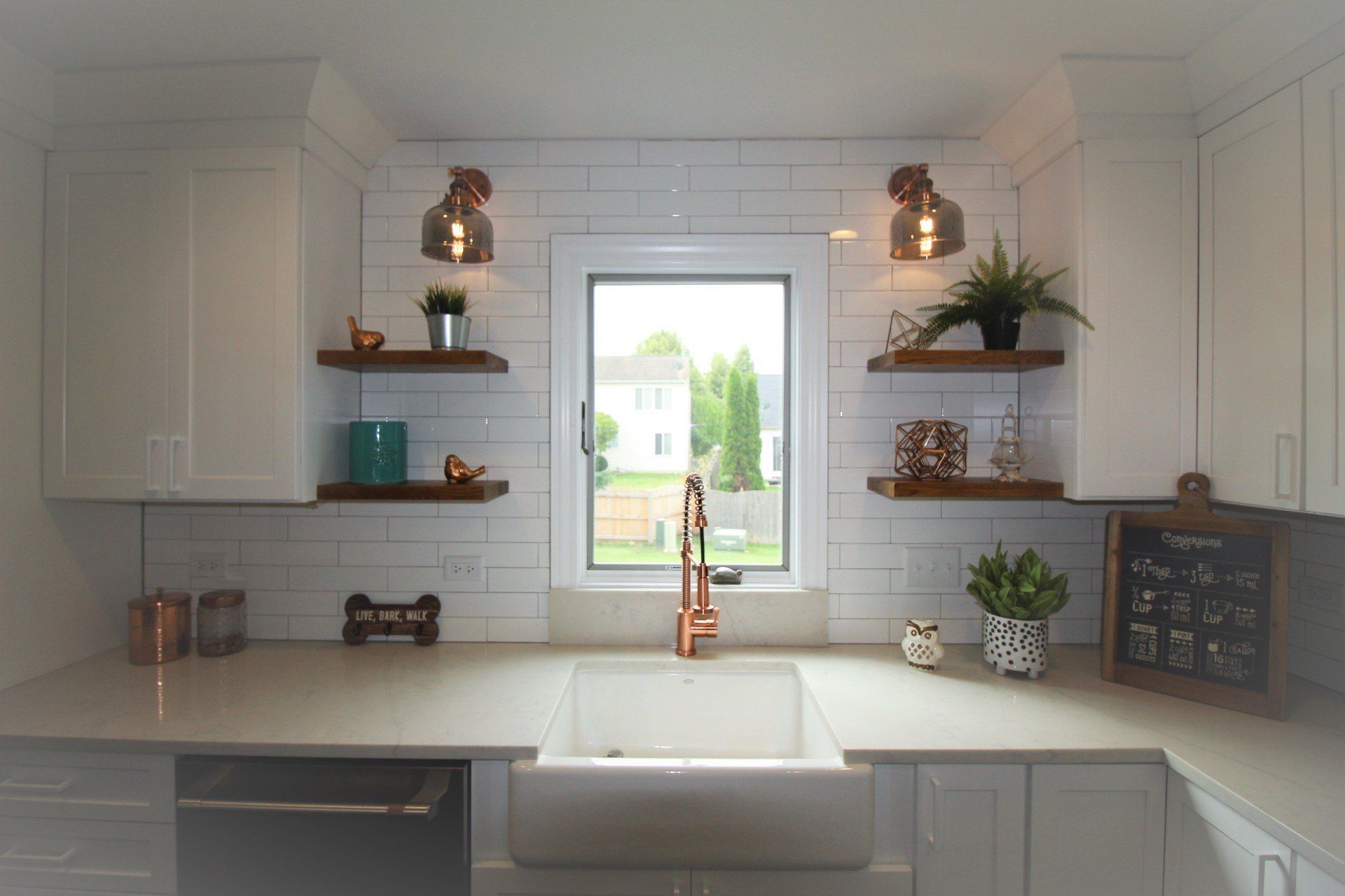A kitchen with white cabinets , a sink , and a window.