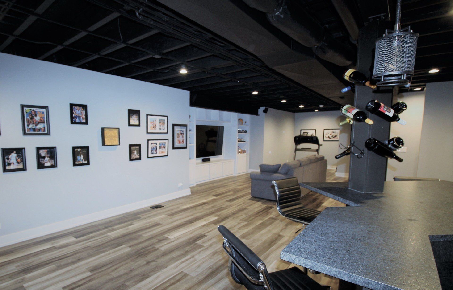 A basement with a bar , chairs , pictures on the wall and a wine rack.
