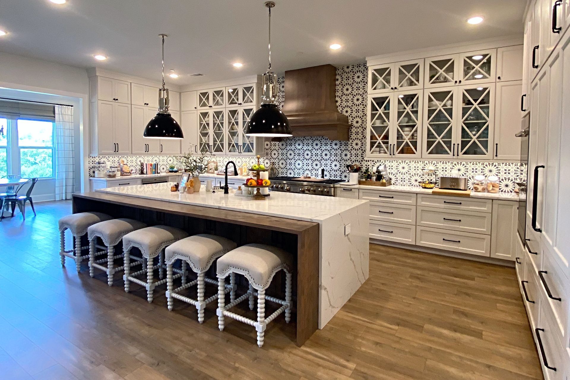 A kitchen with white cabinets , stools , a large island and a stove.