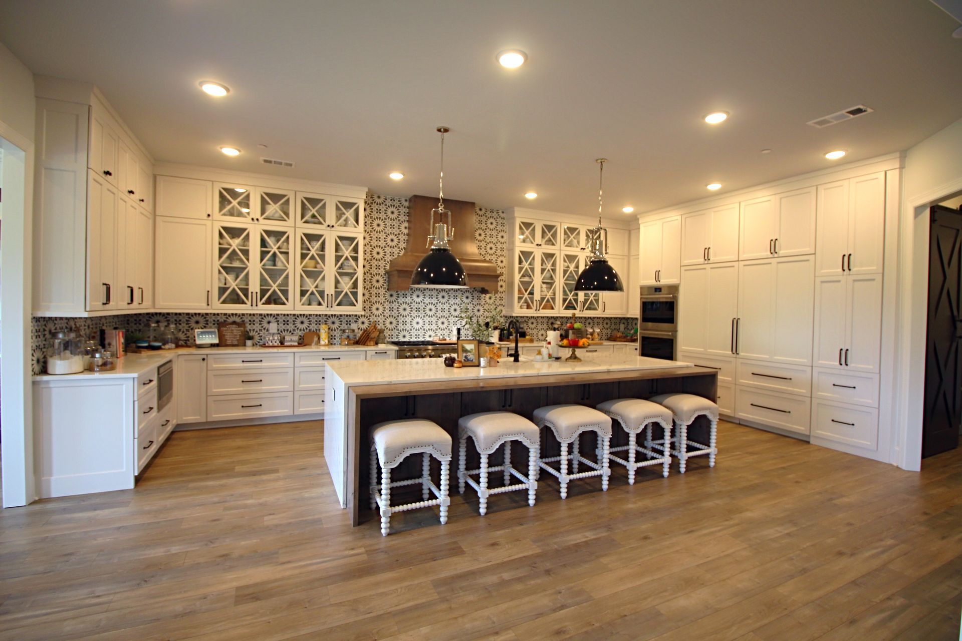 A kitchen with white cabinets , wooden floors , stools and a large island.