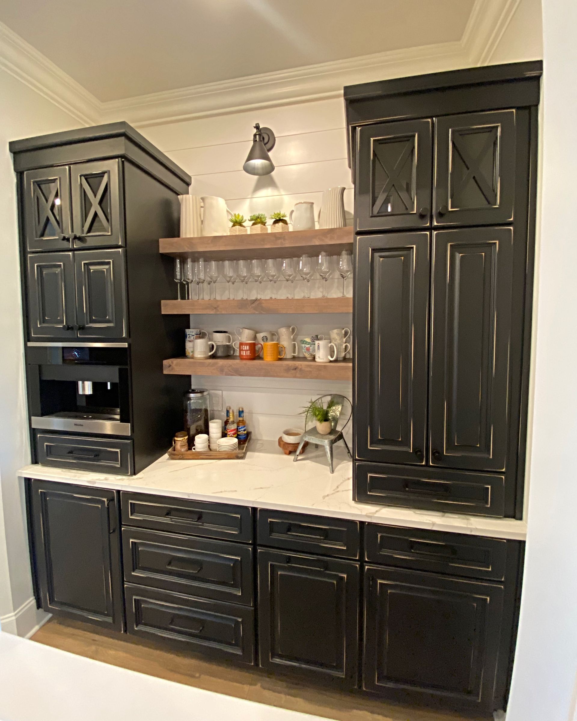 A kitchen with black cabinets , white counter tops , and a coffee maker.