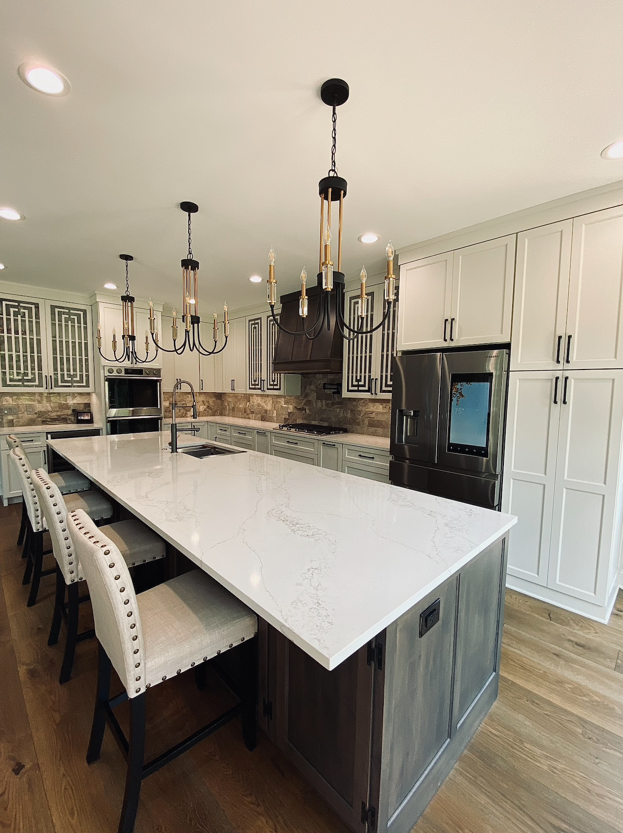 A kitchen with white cabinets , a large island , and a refrigerator.