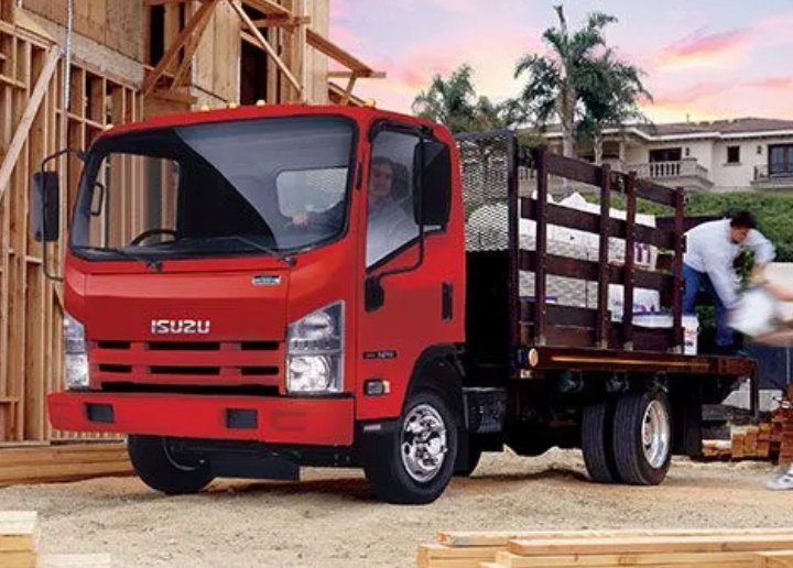 A red isuzu truck is parked in front of a building under construction