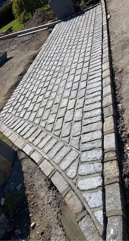 A person is pouring concrete on a sidewalk with a shovel.