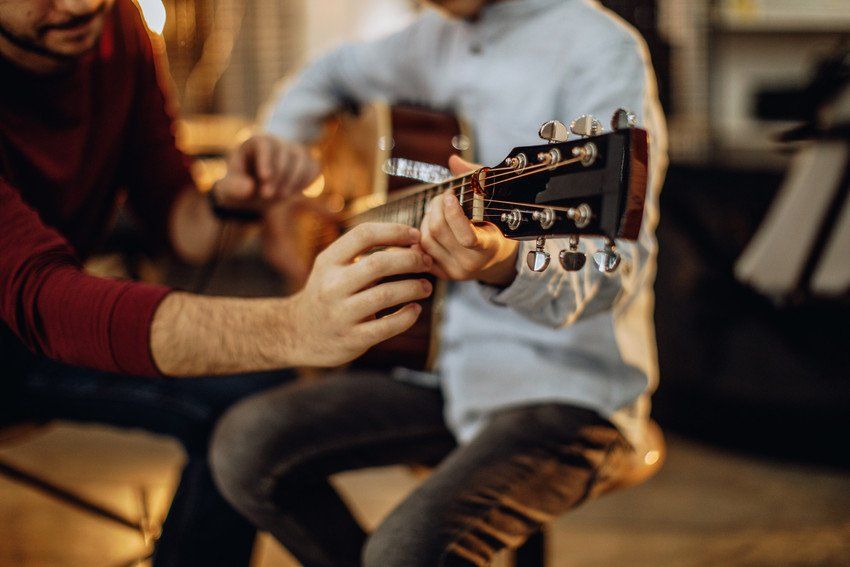 Man guitar teacher working with little boy on guitar lessons