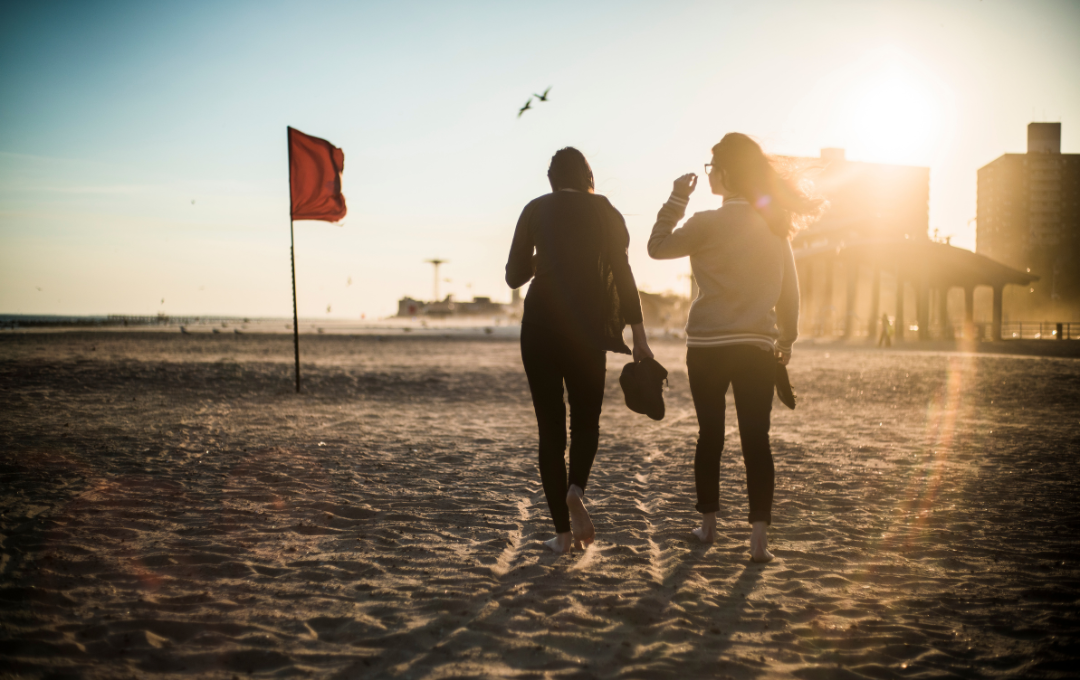 friends walking on the beach with seagull and sun flare in the frame