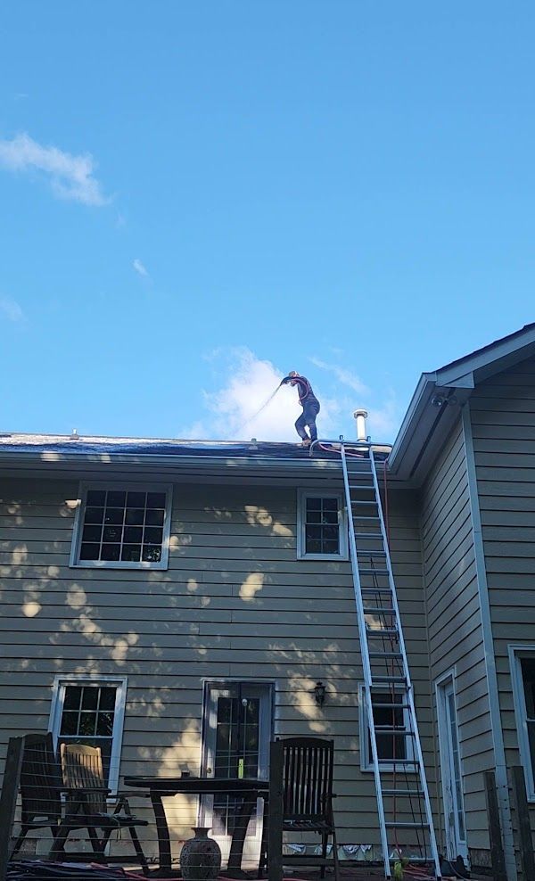 A man is standing on a ladder on the roof of a house.