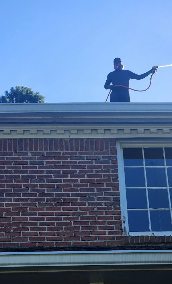 A man is spraying water on the roof of a brick building.