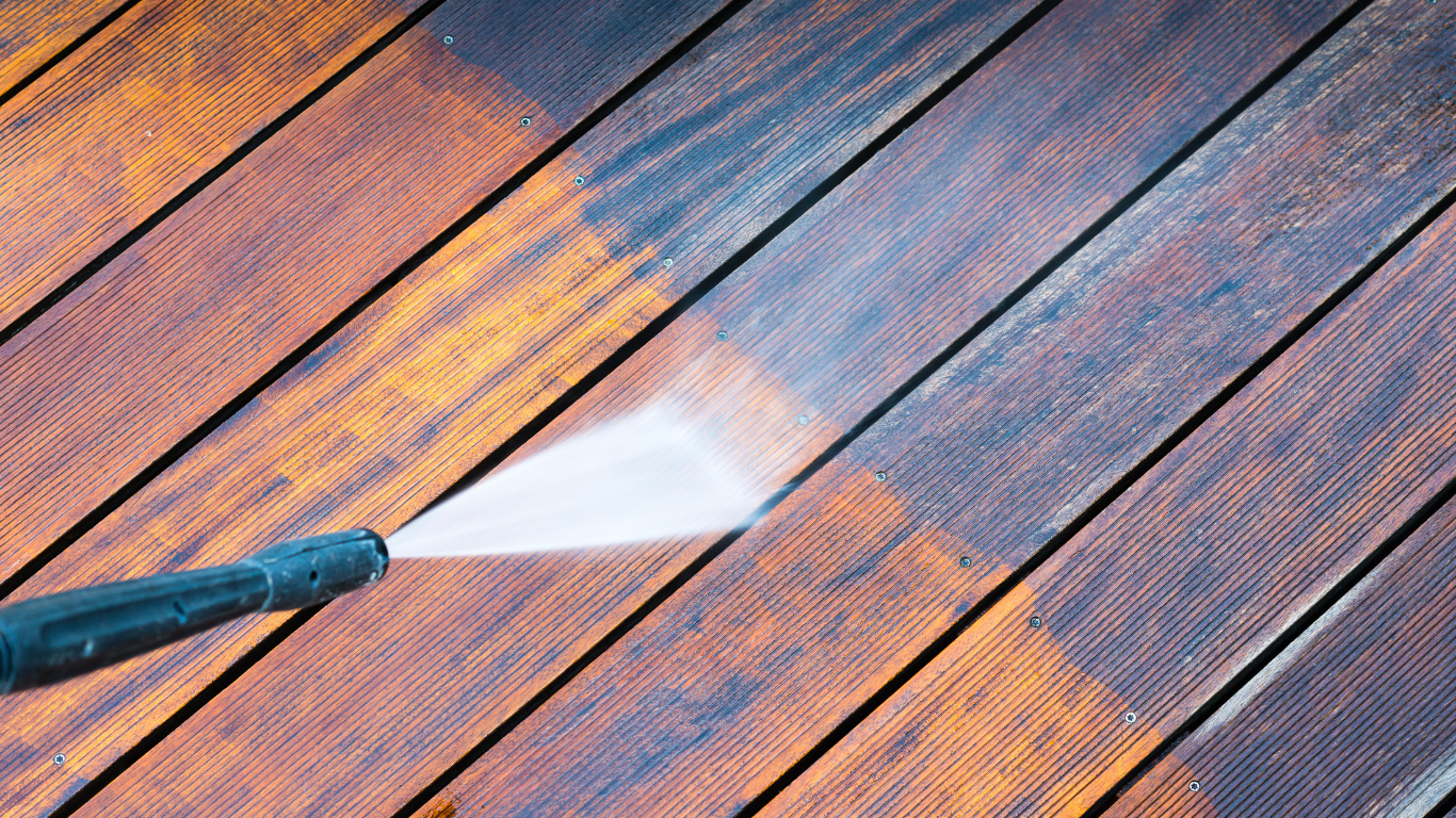 A person is using a high pressure washer to clean a wooden deck.