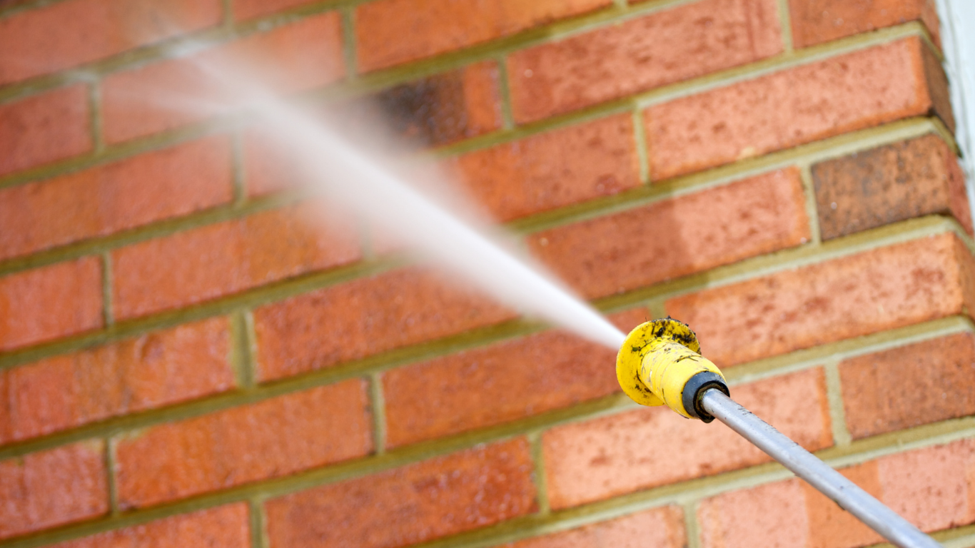 A person is using a high pressure washer to clean a brick wall.