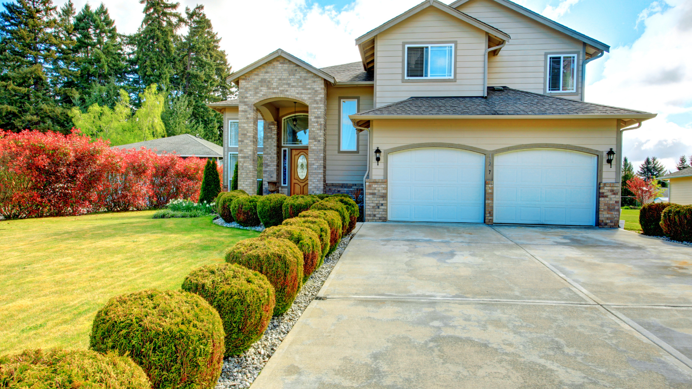 A large house with two garage doors and a lush green lawn.
