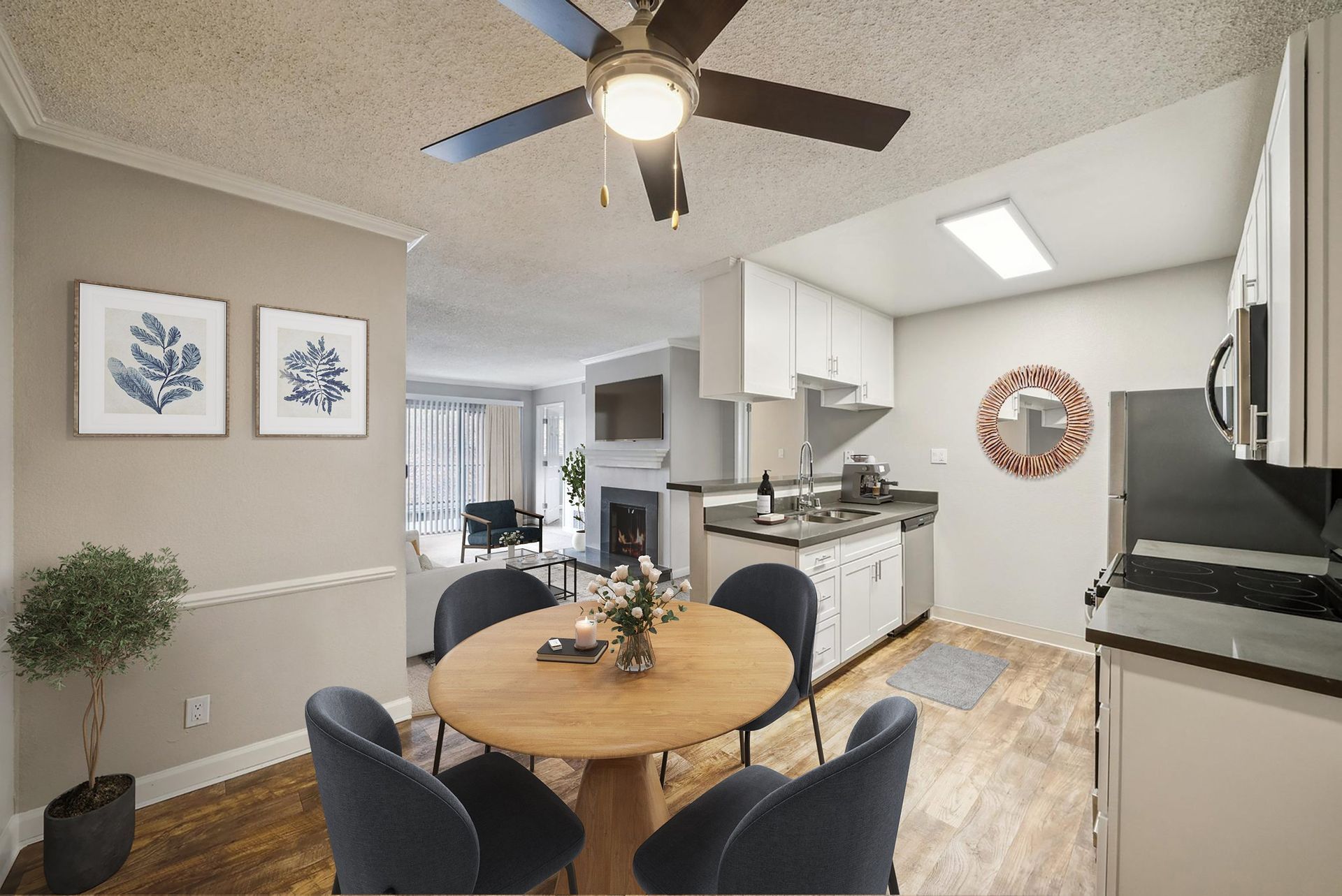 Open-concept apartment kitchen and dining area with white cabinets and a round wooden table.