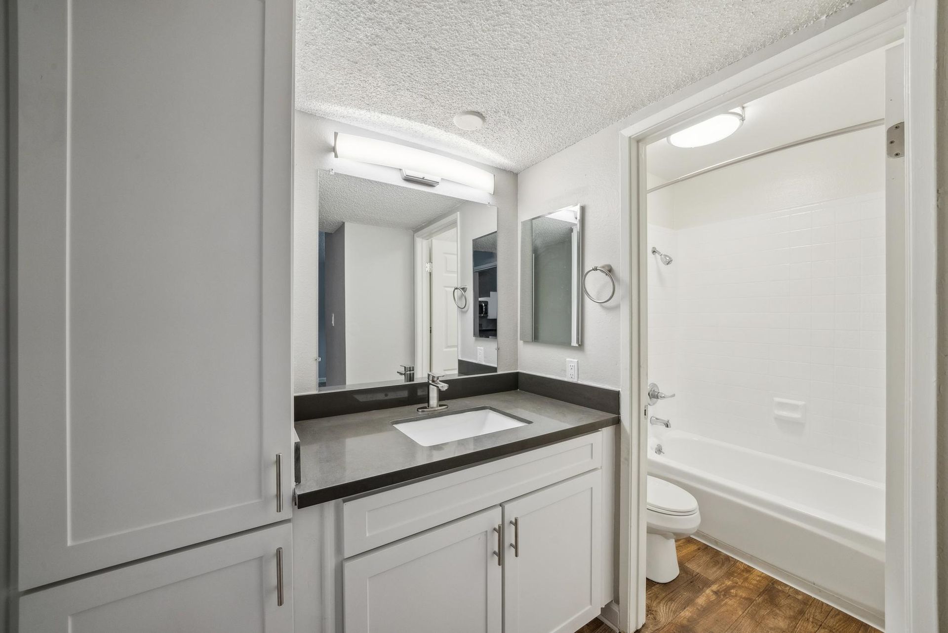 Bathroom vanity with white cabinets, dark countertop, and a tub/shower combo.