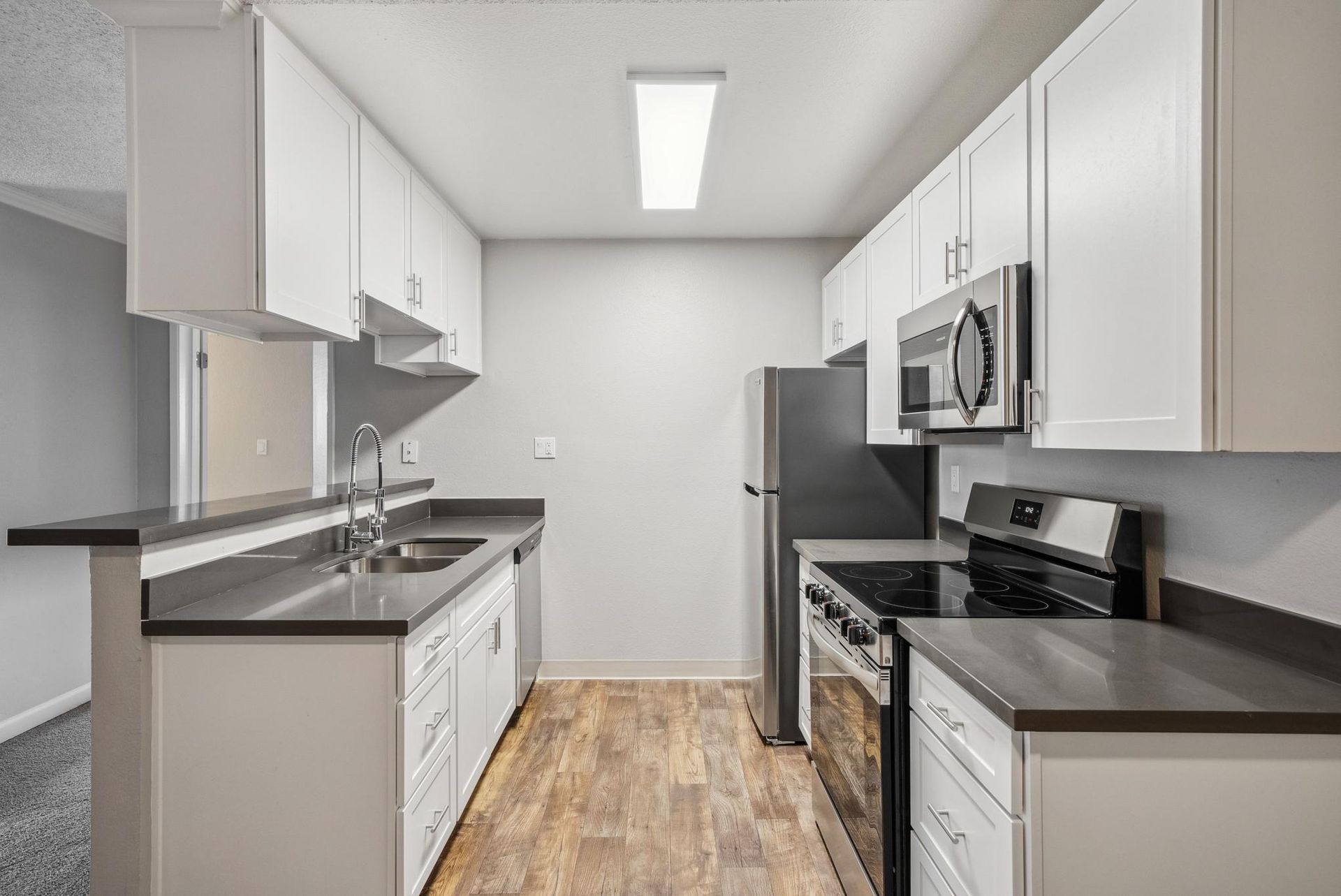 Modern apartment kitchen with white cabinets, stainless steel appliances, and a double-basin sink.
