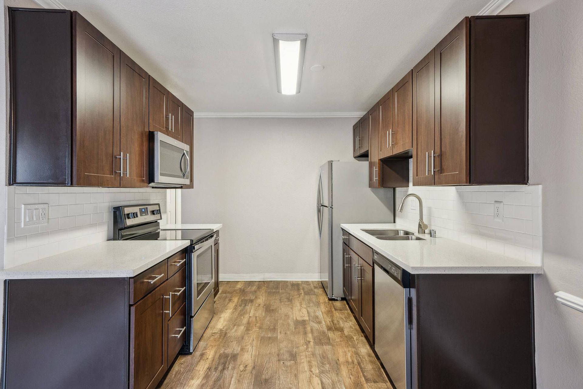 Kitchen with dark wood cabinets, white countertops, and stainless steel appliances.