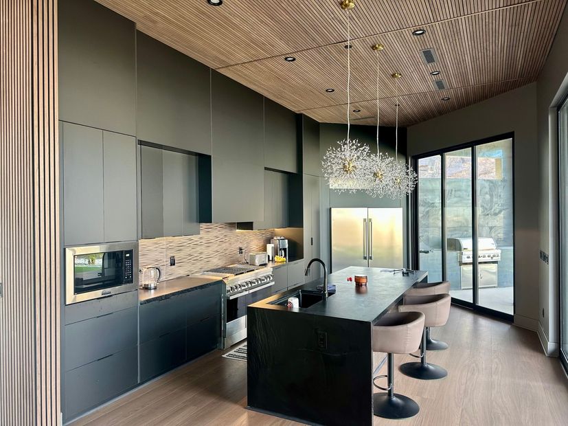 Modern kitchen with dark cabinetry, black island, bar stools, and large glass doors to a bright view