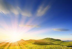 Rays of sunlight across a blue sky over hills