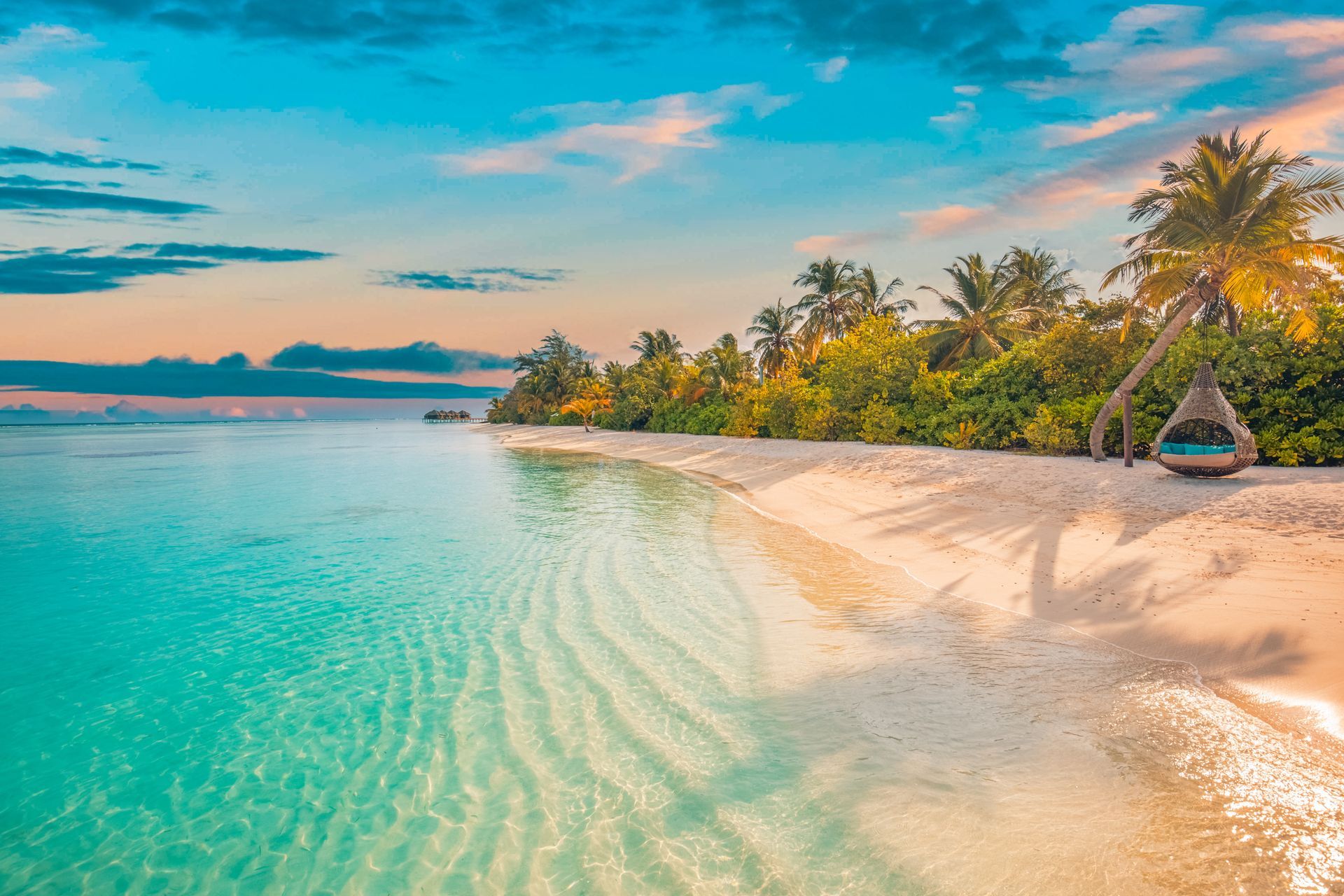 Tropical beach with turquoise water, white sand, palm trees, and a sunset sky