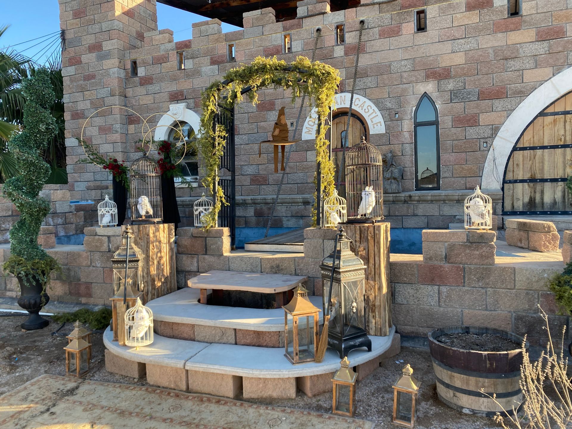 Stone castle facade with archway decorated with greenery. Lanterns on steps.