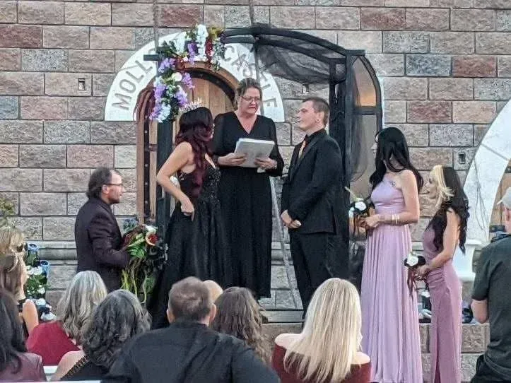 Wedding ceremony at a stone castle; couple with officiant and attendants; guests watch.