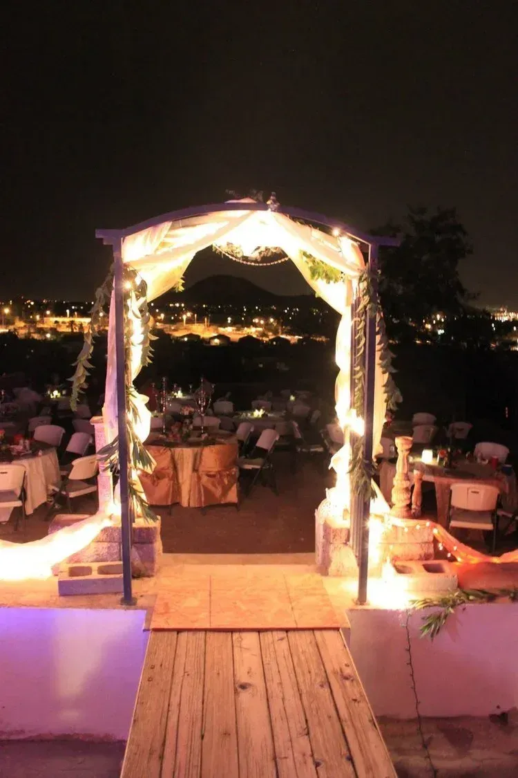 Wooden archway with lights, leading to a wedding reception at night overlooking city lights.