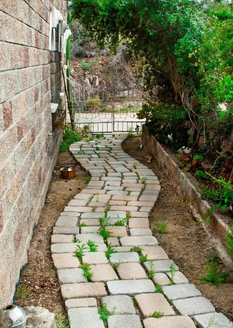 Brick pathway curves between a brick wall and foliage, leading to a gate.