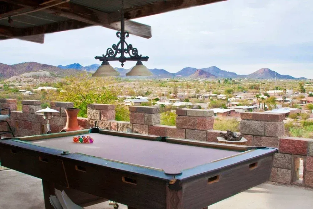 Pool table on a patio overlooking a landscape with mountains in the distance; overhead light fixture.