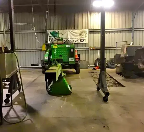 A Green Tractor With a Log Splitter in a Metal Workshop — Amazon Tree Service in Picton, NSW