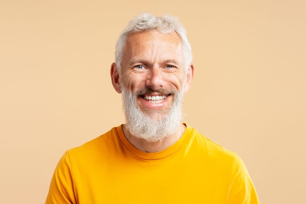 A man with a beard and a yellow shirt is smiling.