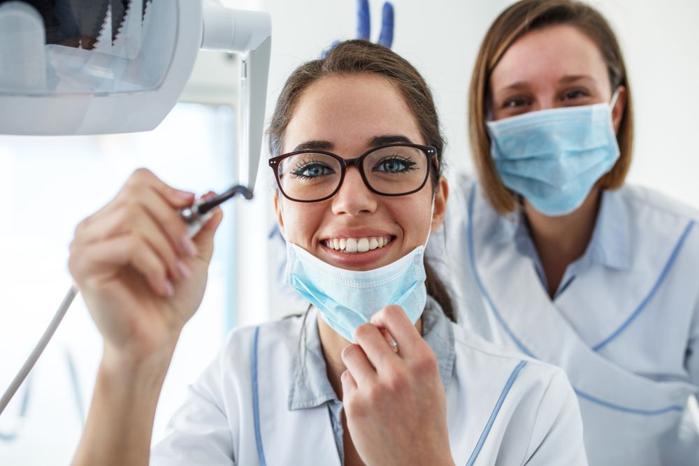 Two female dentists wearing face masks are smiling in a dental office.