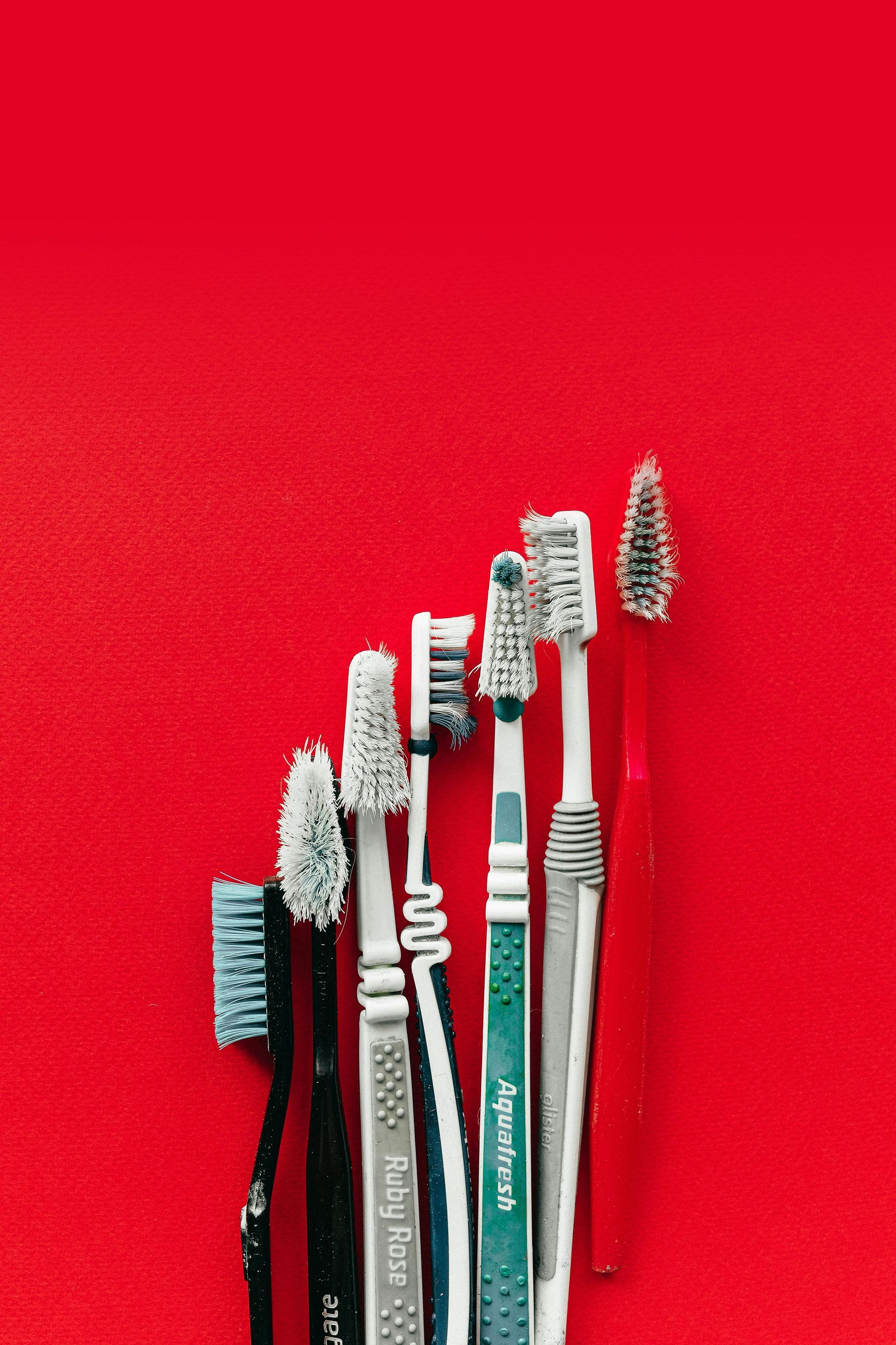 Toothbrushes with worn bristles, lined up on a red background.