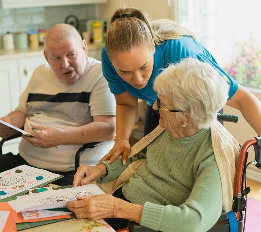 Caregiver assists two seniors with crafts in a home.