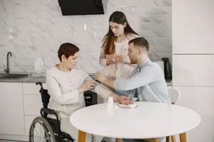 Person in wheelchair receiving injection in kitchen, assisted by two others.