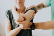 A person's elbow is being examined by another person, indoors.