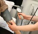 A person's arm with a blood pressure cuff. A healthcare worker takes the reading with a stethoscope and gauge.