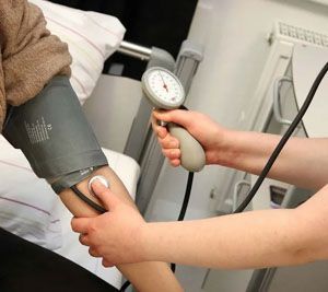A person's arm with a blood pressure cuff. A healthcare worker takes the reading with a stethoscope and gauge.