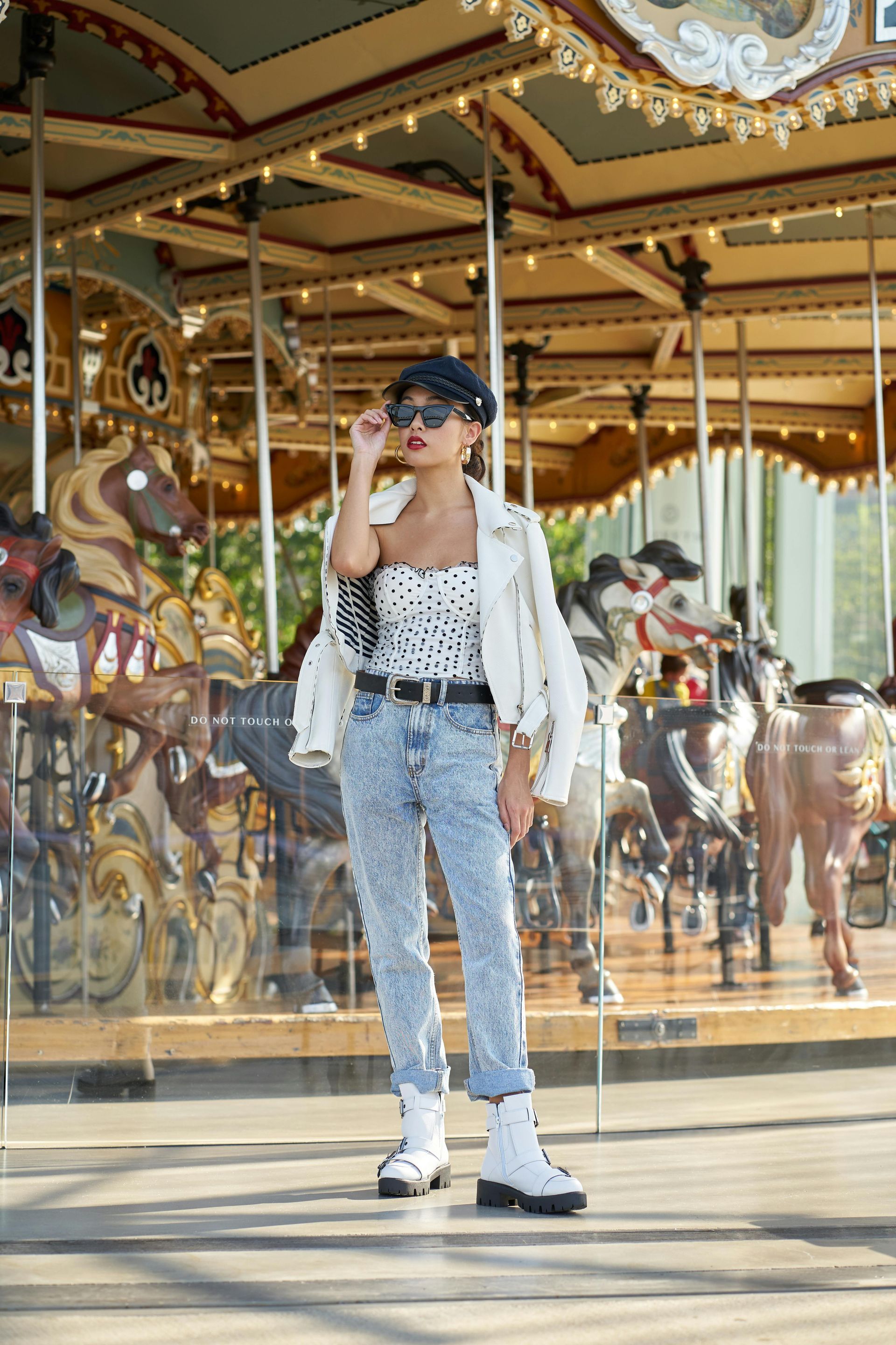 A woman is standing in front of a merry go round.