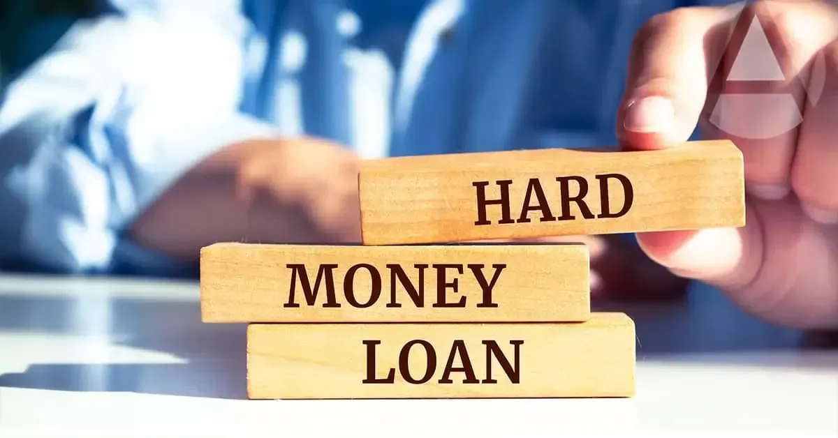 A person in professional attire holds a key above a model house sitting on a clipboard at a desk.