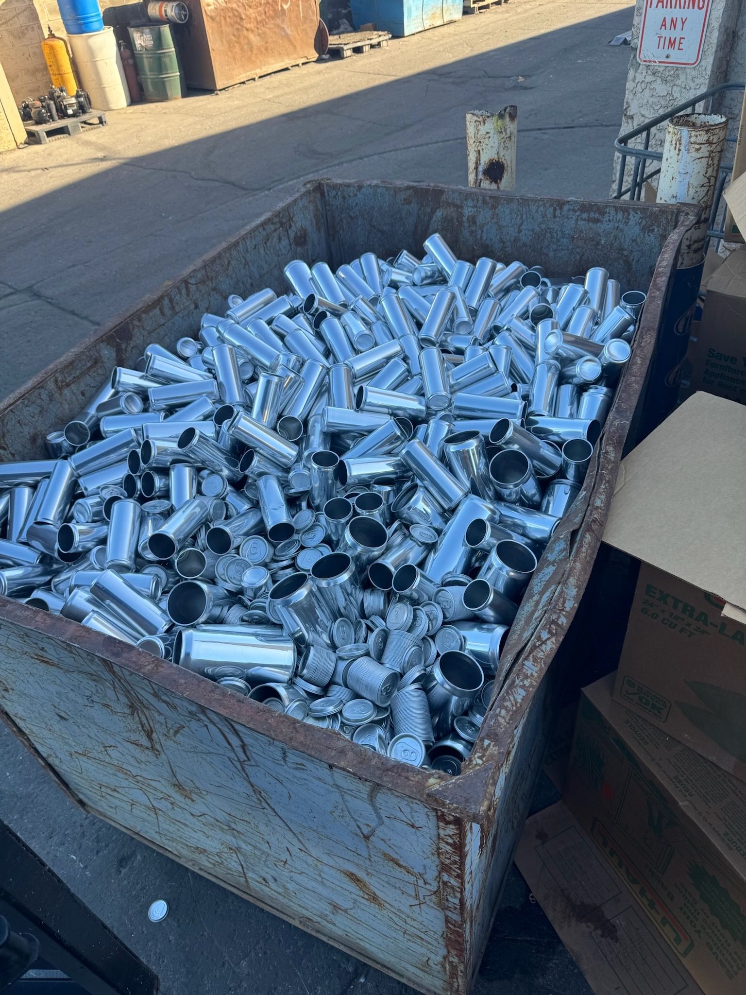 Metal recycling bin filled with silver aluminum cans in an outdoor setting.