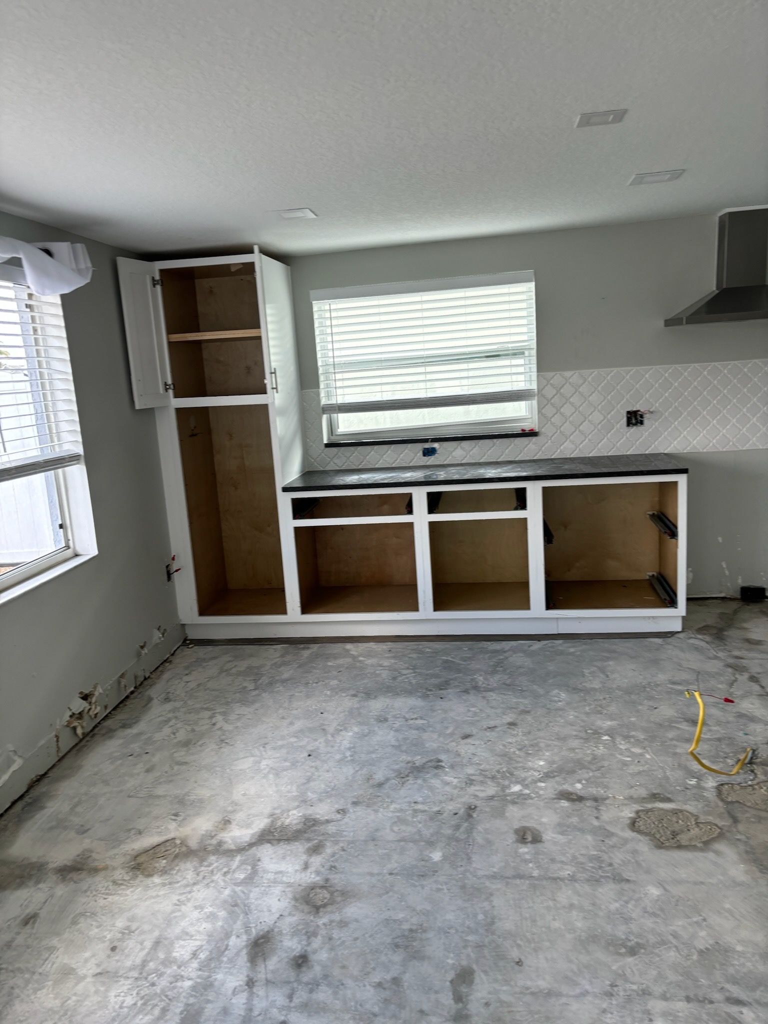 Kitchen renovation: unfinished cabinets, dark countertop, and exposed concrete floor.