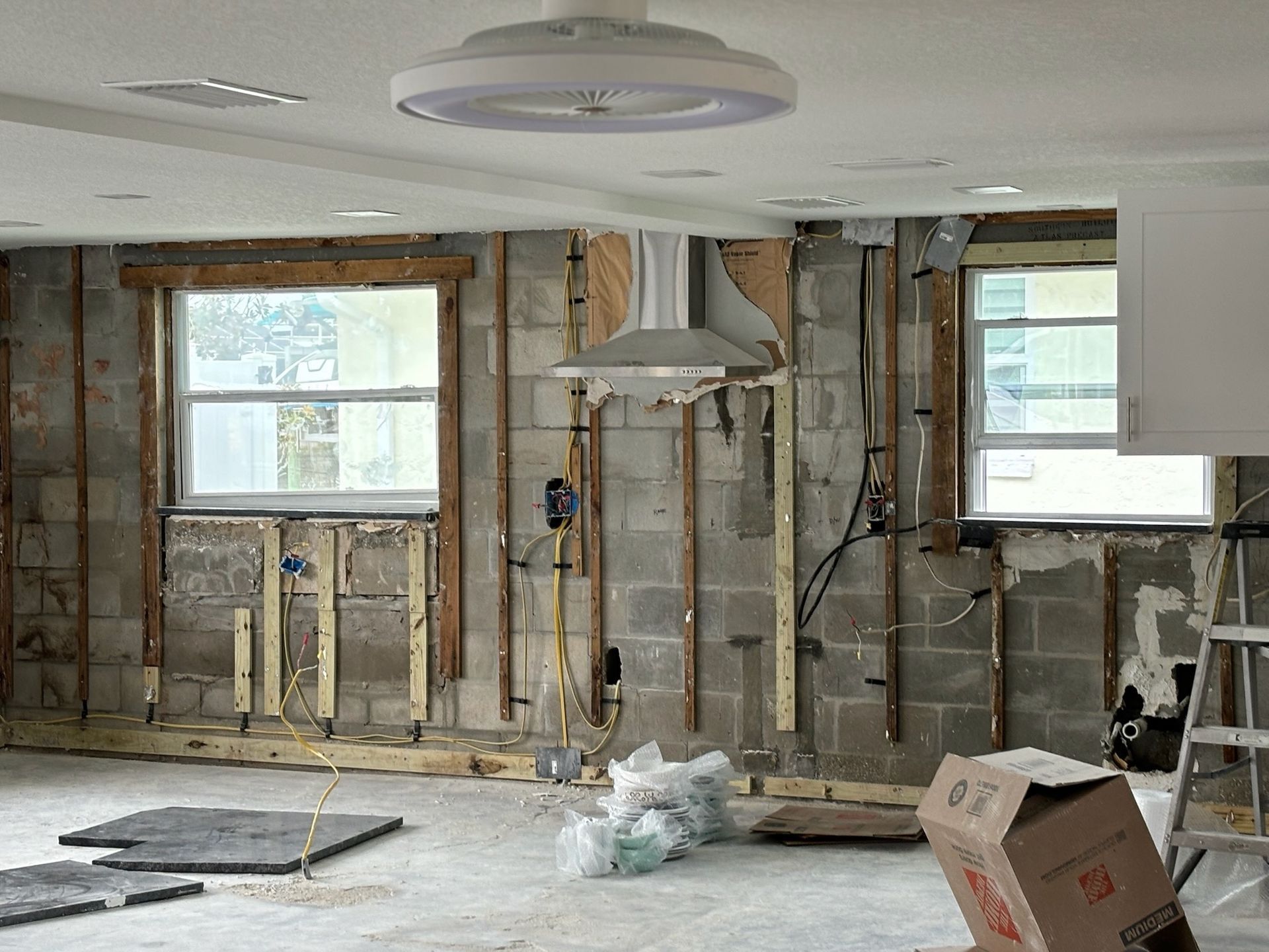Interior view of a room under renovation, with exposed cinder block walls, windows, and ceiling fan.