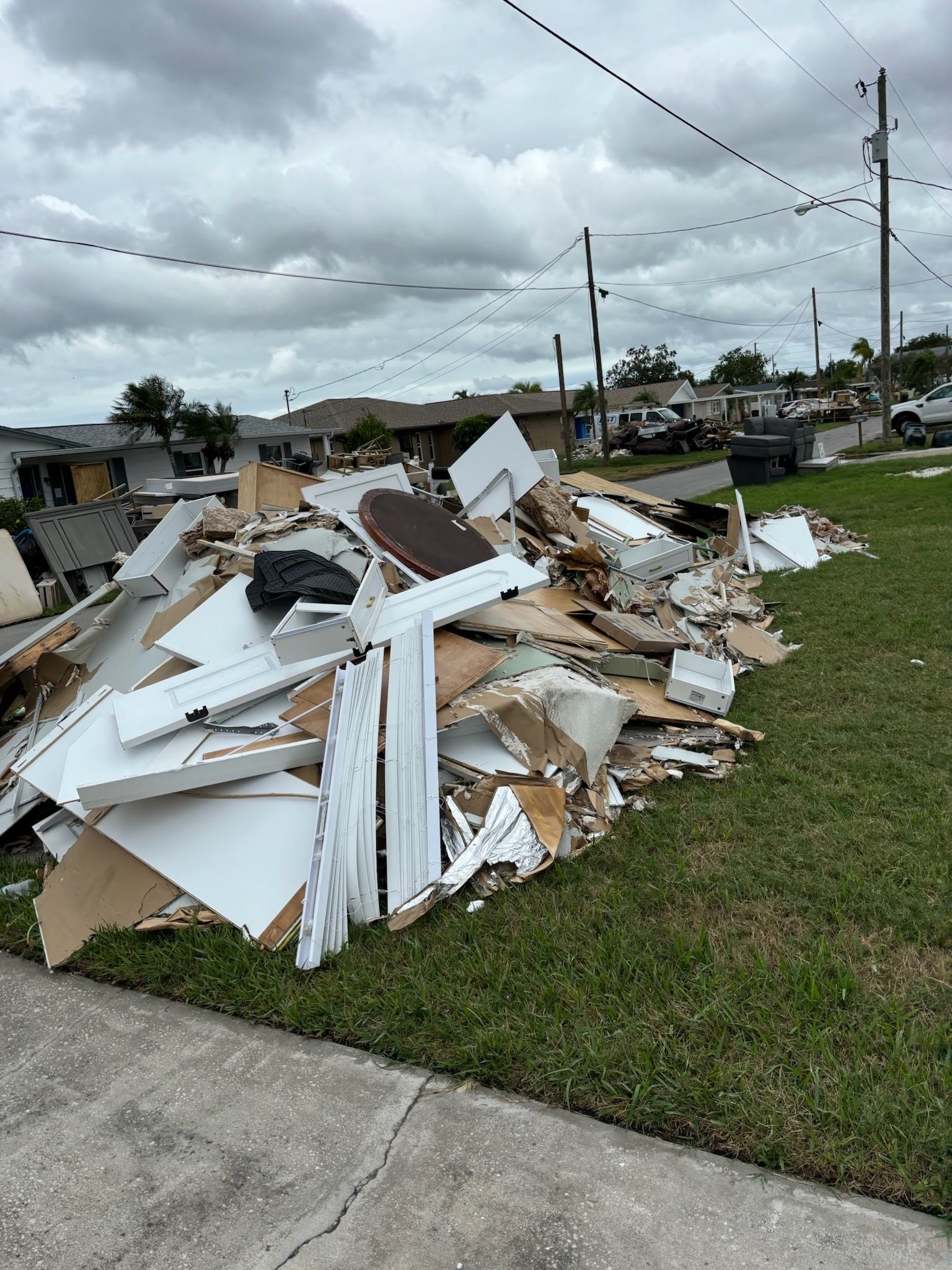Pile of storm debris on a lawn, including white wood and cardboard against a cloudy sky.