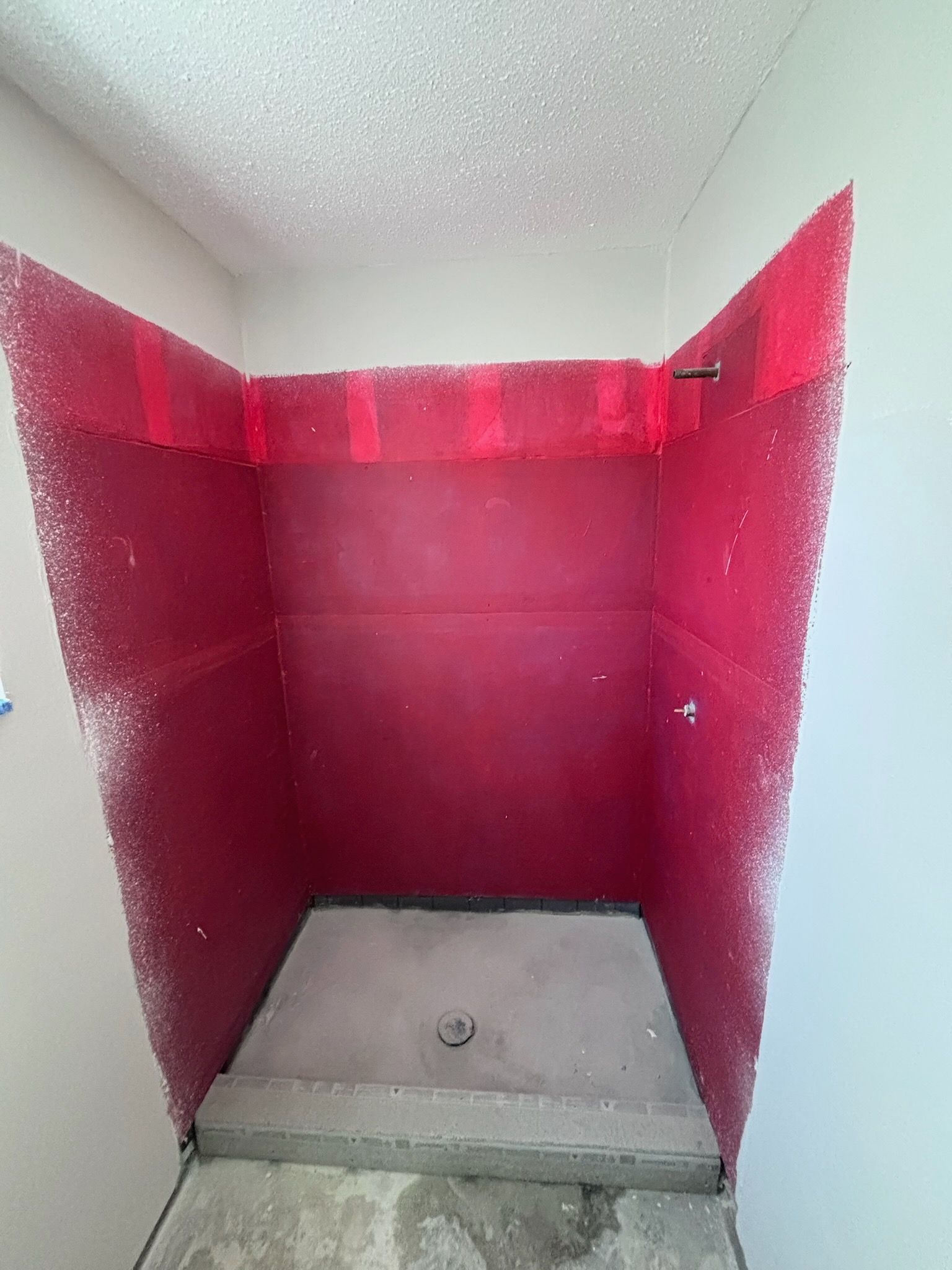Red waterproof shower stall with concrete base and drain, angled walls, and textured ceiling.
