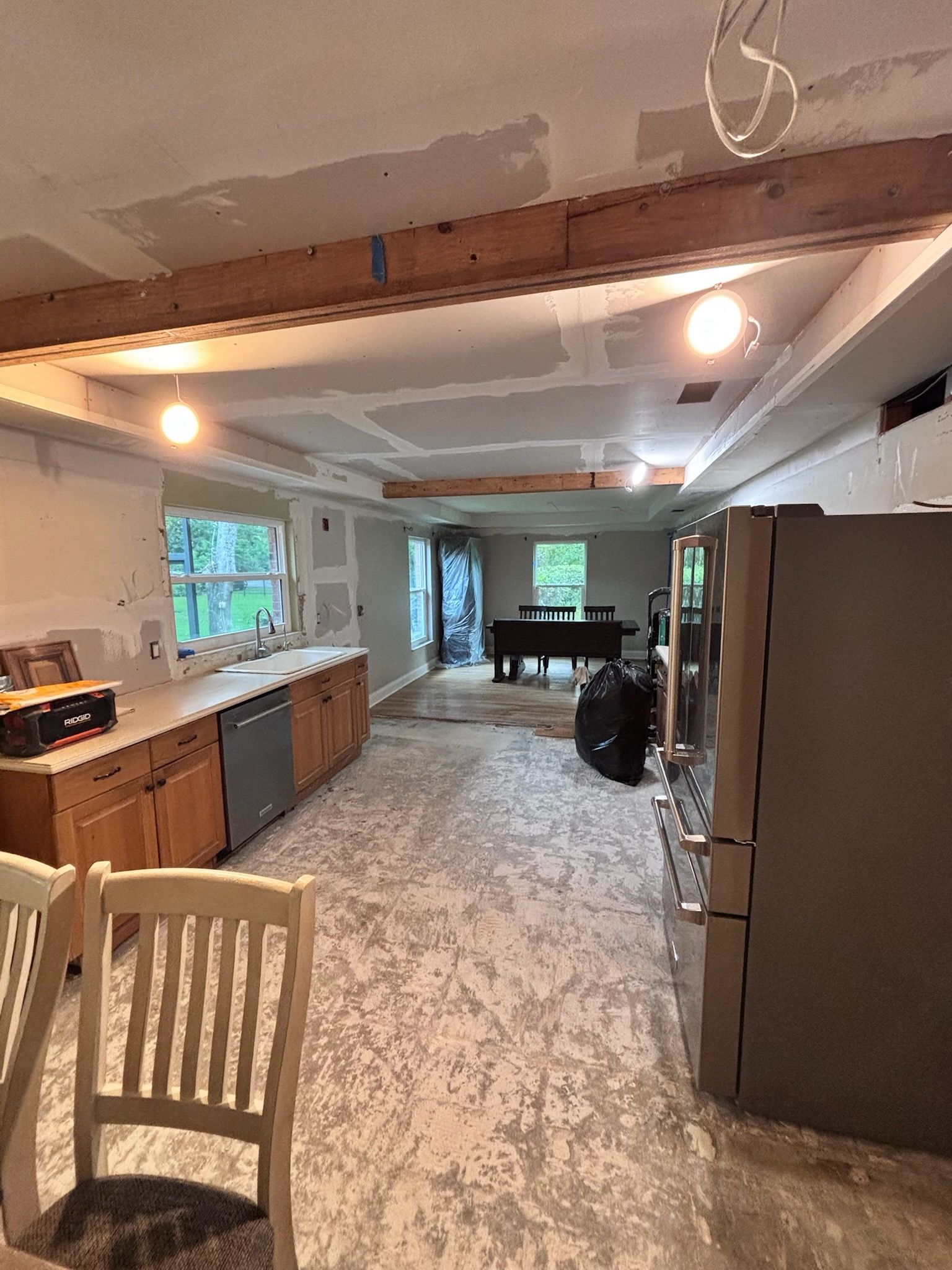 Kitchen under construction with exposed beams, cabinets, appliances, and unfinished flooring.