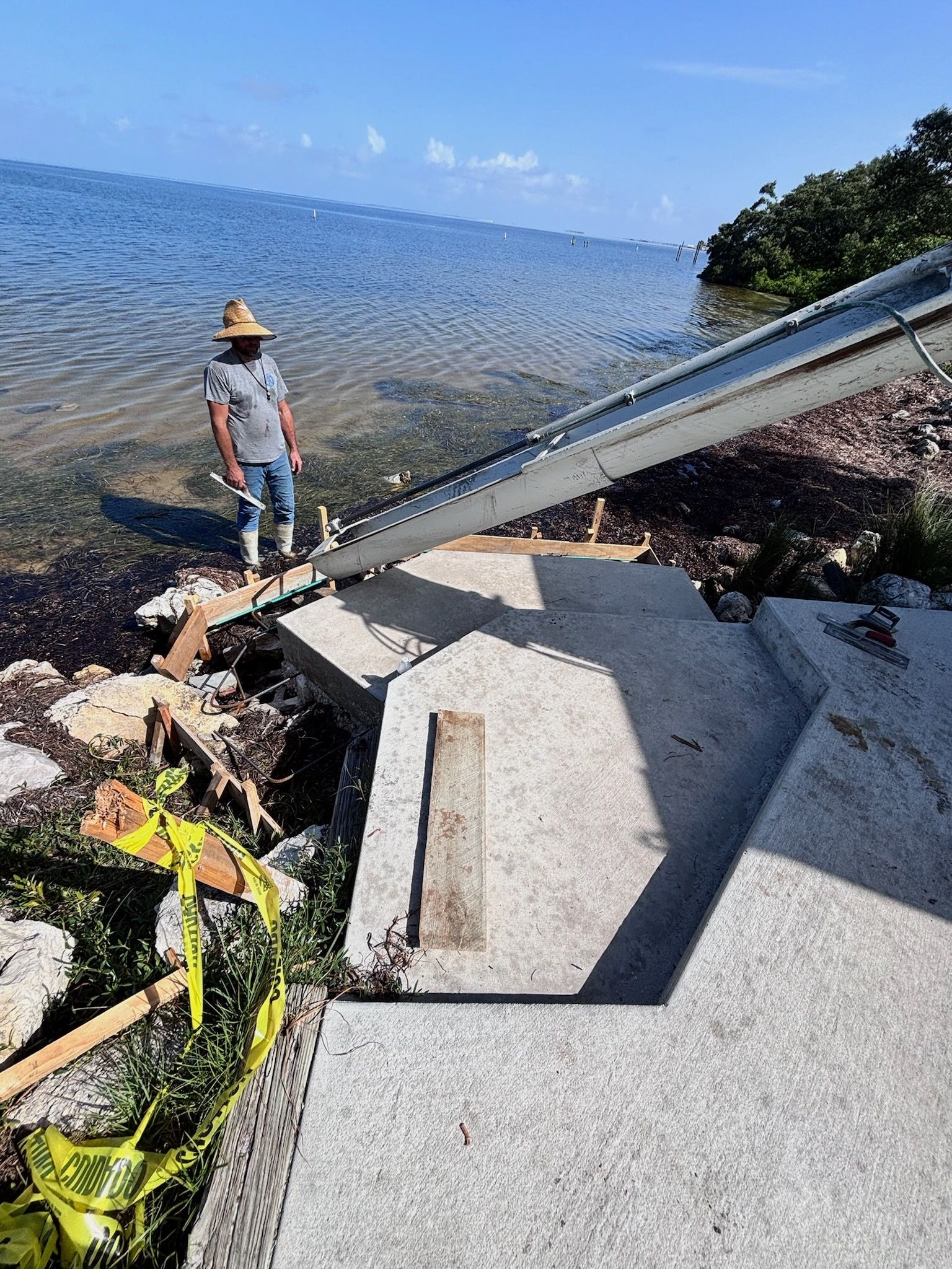 Man standing near damaged concrete steps leading to the ocean; construction in progress; safety tape visible.