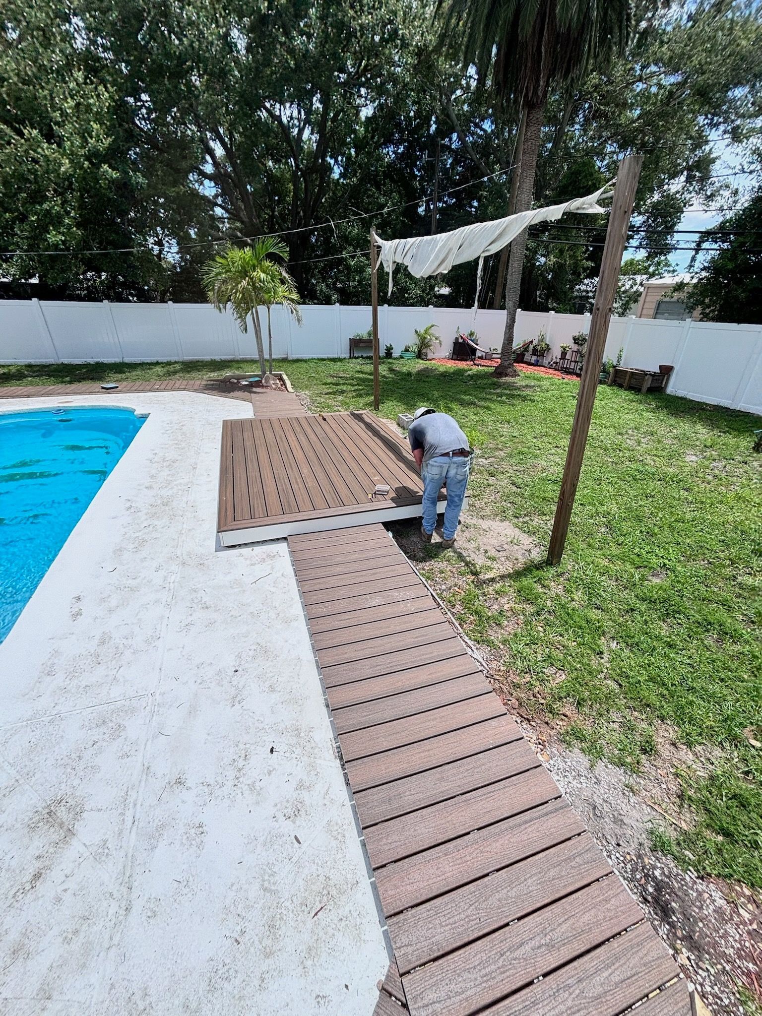 Person installing wooden walkway next to a pool in a backyard.