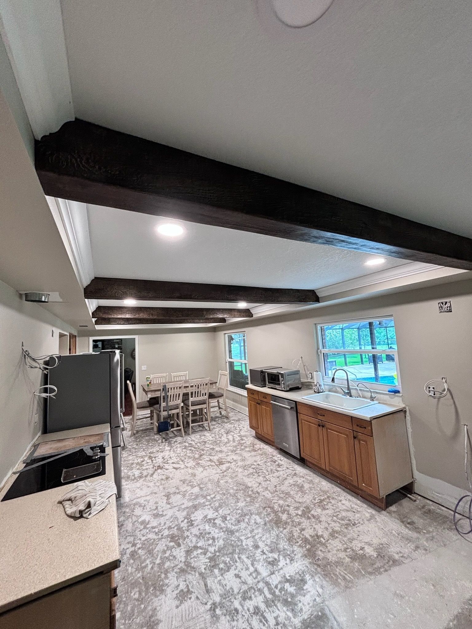 Interior view of a kitchen with dark wooden beams, light-colored countertops, and a dining area visible in the distance.