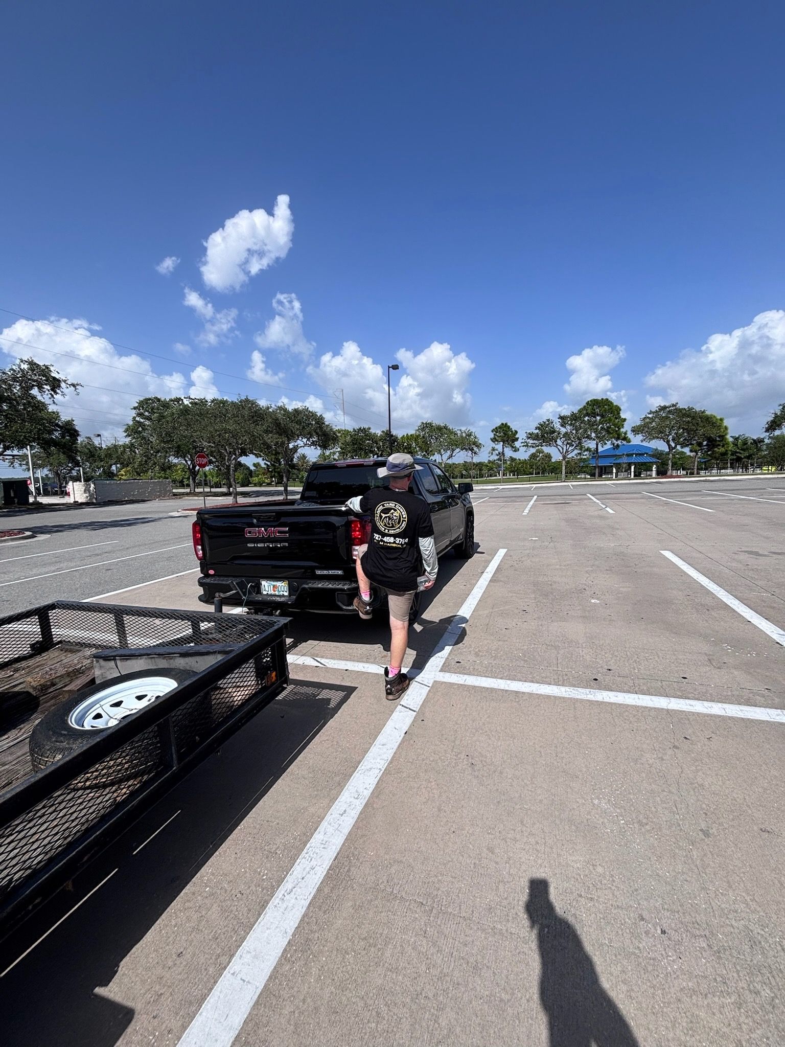 Man walking in parking lot towards black truck with trailer on a sunny day.