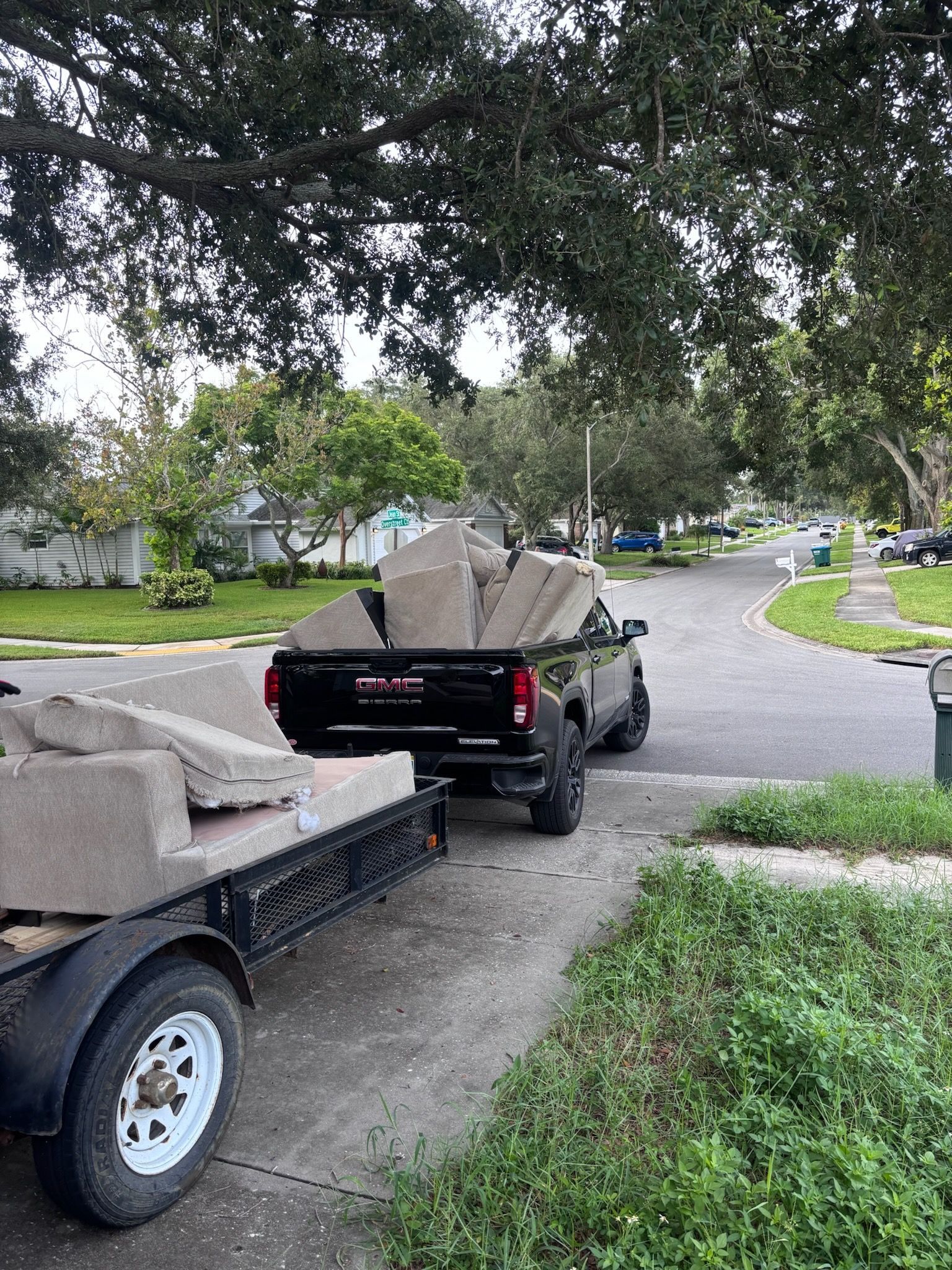 Black truck pulling a trailer loaded with large concrete slabs on a residential street.