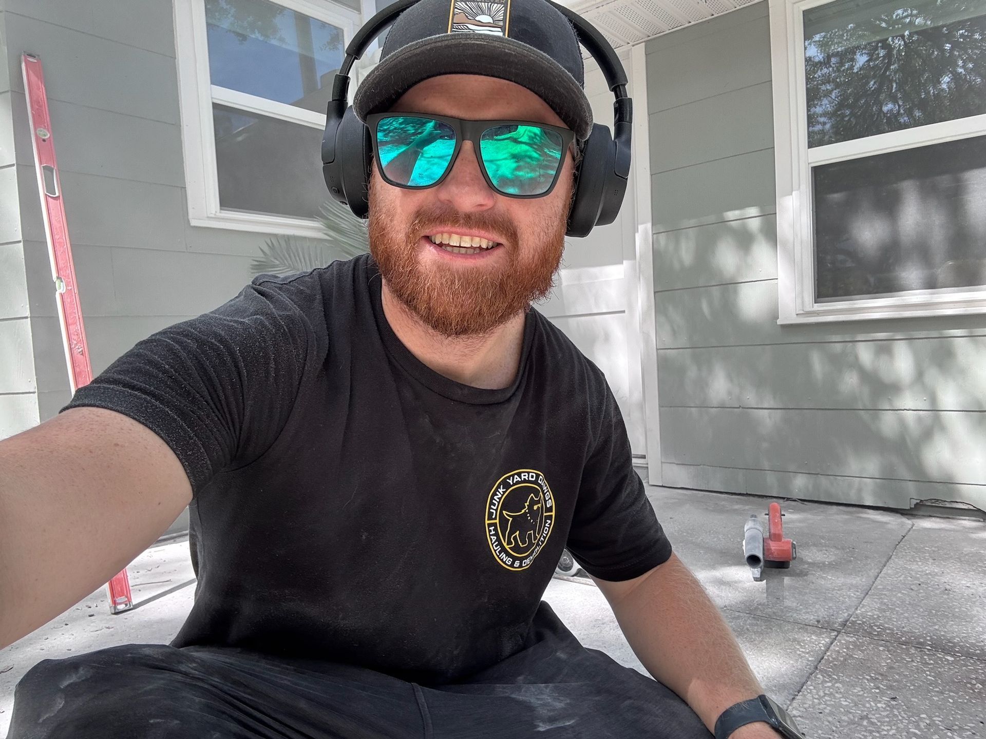 Man with beard and sunglasses, wearing headphones, crouched outdoors working on concrete.